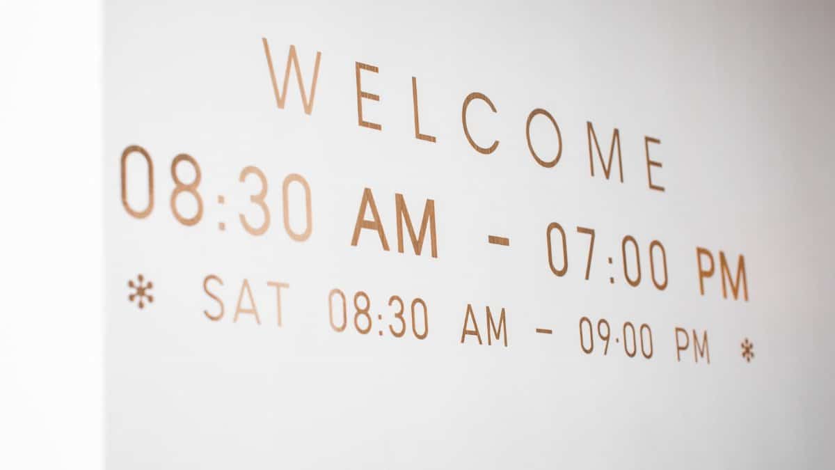 Close-up of a minimalist welcome sign displaying business hours in stylish typography.