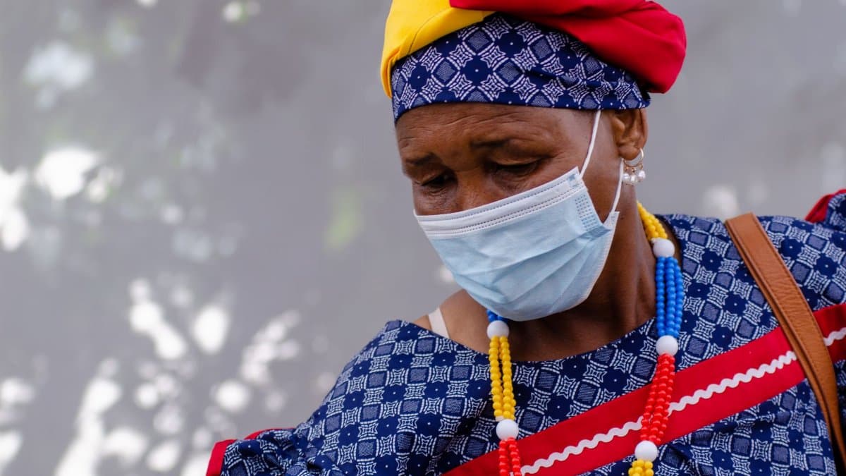 Senior woman wearing a face mask and vibrant traditional clothing outdoors during the day.