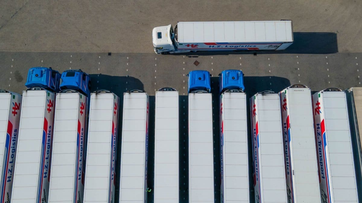 Top-down drone shot of logistics trucks arranged in a row in a parking lot.