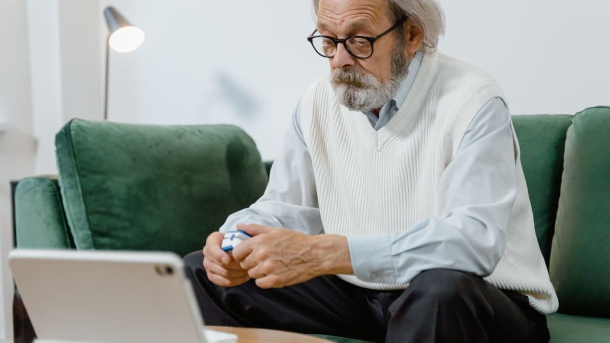 Elderly man sitting on couch, using a pulse oximeter for health monitoring.
