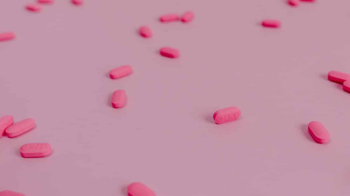 A flat lay of vibrant pink pills scattered on a pastel pink surface, perfect for healthcare themes.