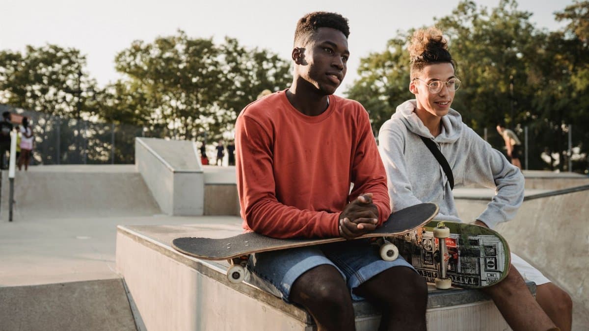 Two young men enjoying a sunny day at a skatepark with their skateboards.
