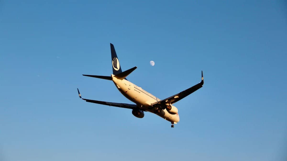 Airplane in flight against a clear blue sky with the moon visible, showcasing aviation travel.