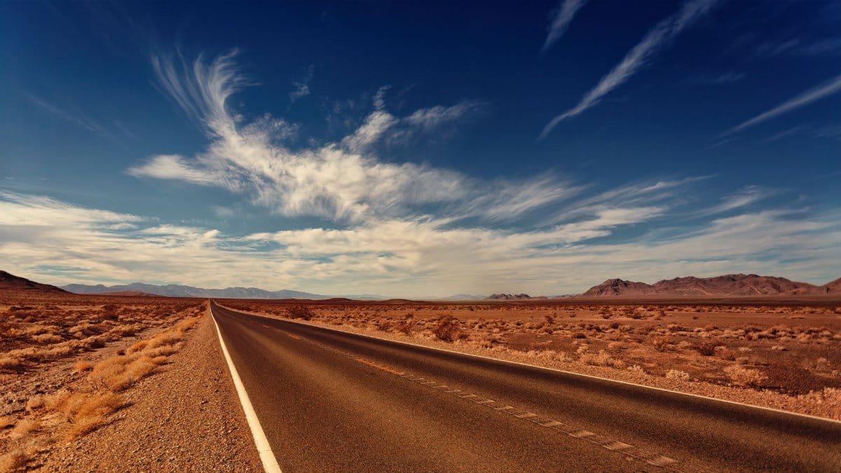 Long desert highway stretching into the horizon under a vibrant blue sky and wispy clouds.
