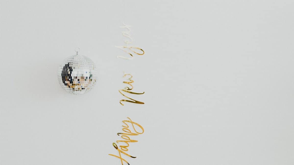 Minimalist New Year decoration with a disco ball and gold text on a light background.
