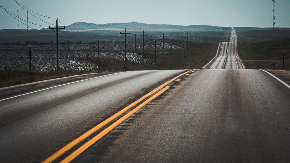 A scenic highway stretches through rolling hills lined with telephone poles and open skies.