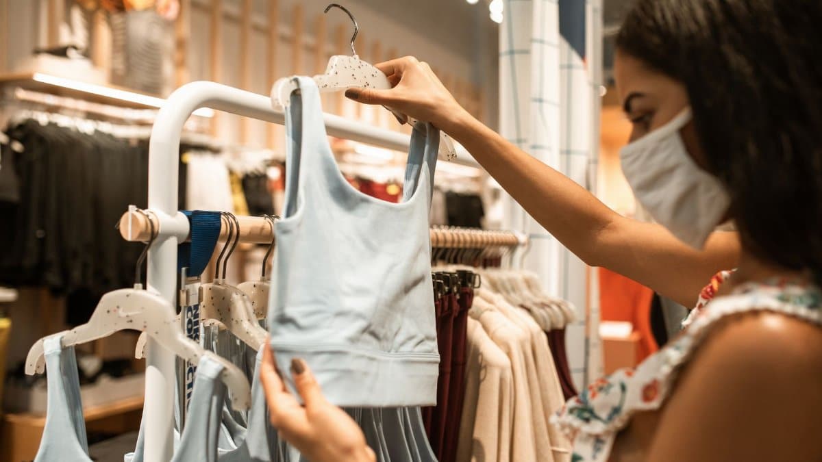 A woman wearing a face mask browses sports bras in an apparel store, embracing the new normal.