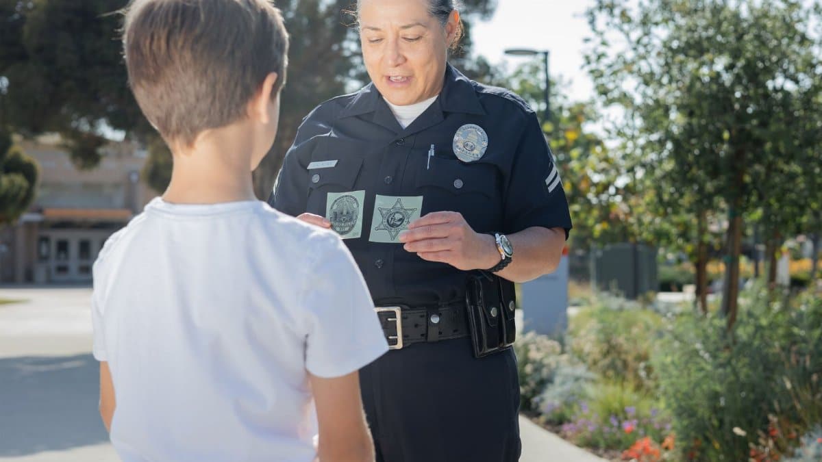 A police officer shows her badge to a child outside in a community setting, fostering trust.