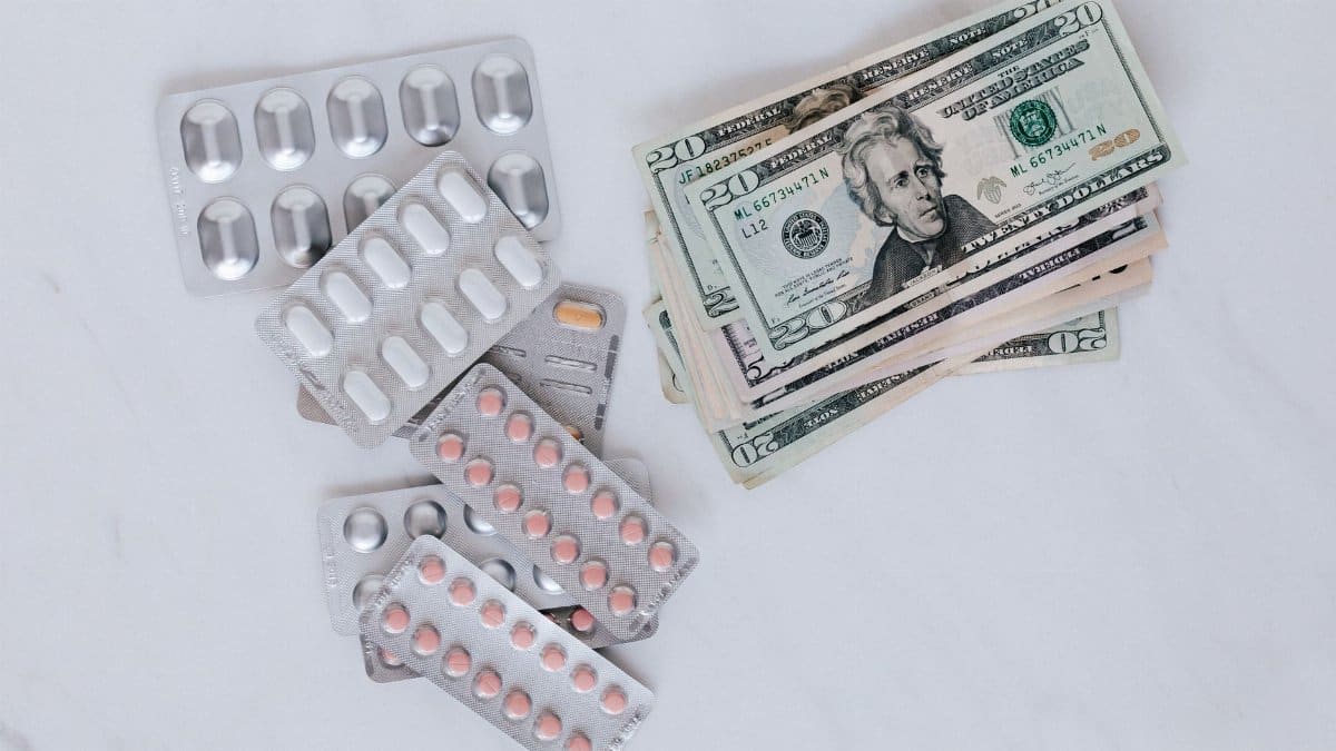 From above of silver blister full of drug near big pile of dollar to spend on medication