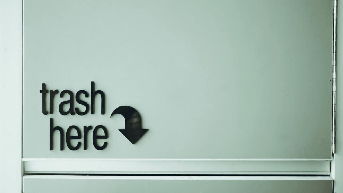 Black inscription with pointer indicating spot for trash disposal on white door of rubbish bin located in light public place