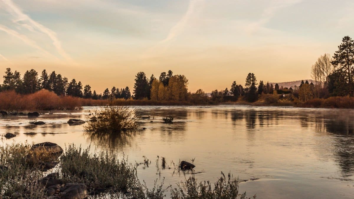 Calm river scene at sunrise with soft orange sky reflecting in the waters of Liberty Lake, Washington.