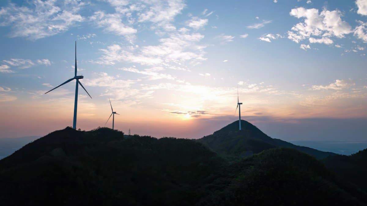 Silhouetted wind turbines on a hilly landscape during sunset, highlighting renewable energy.