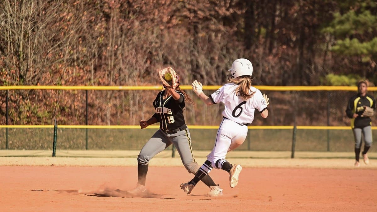 Dynamic action shot of two female softball players on a sunny day in a competitive game.