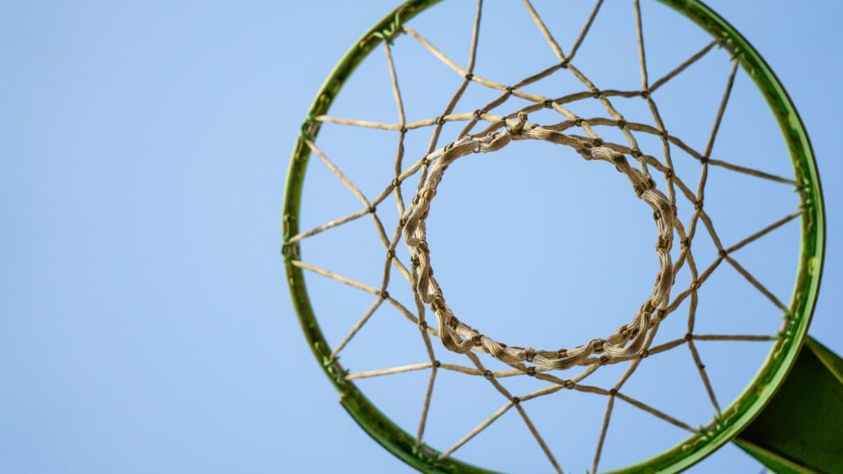 Looking up through a green basketball hoop with netting and a background of clear blue sky.