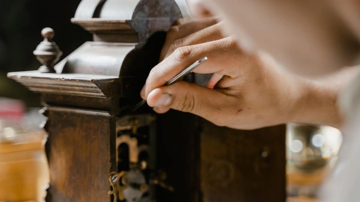 Close-up of hands skillfully restoring an antique wooden clock, highlighting craftsmanship.