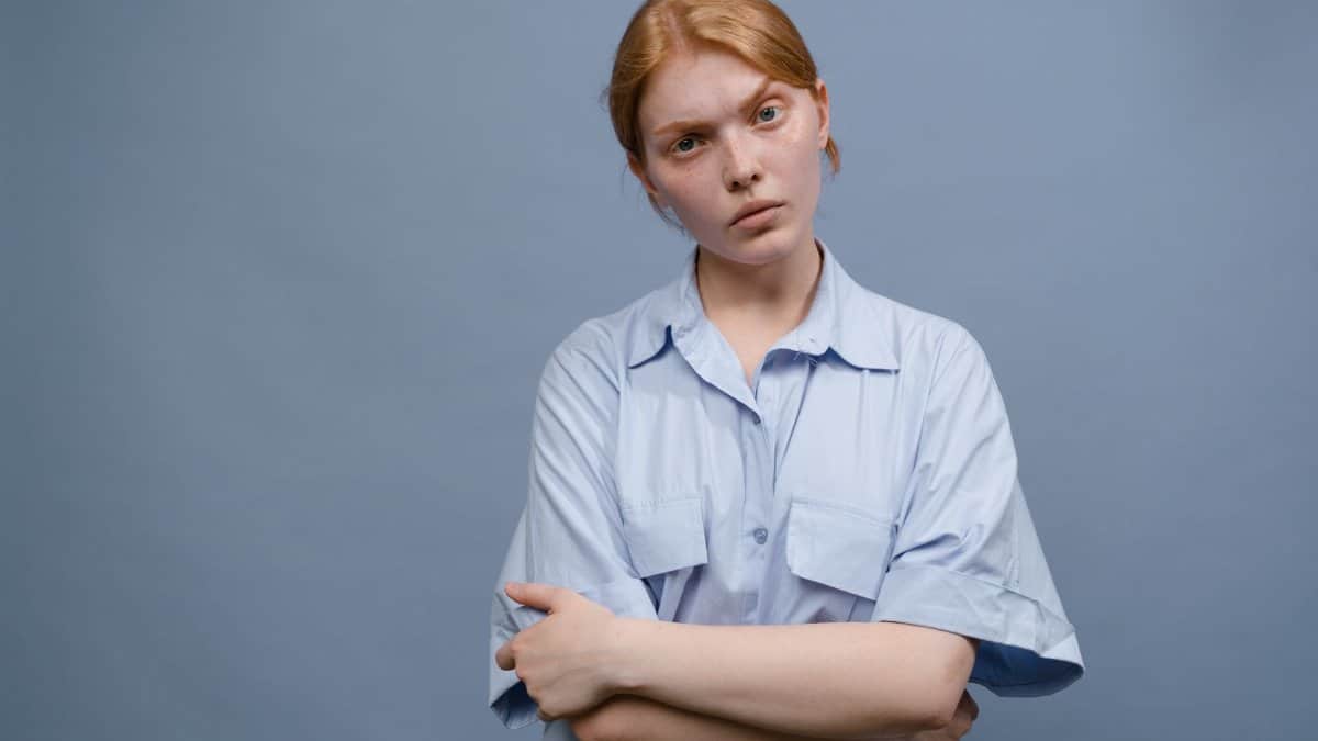 A woman with crossed arms and neutral expression in a simple portrait.