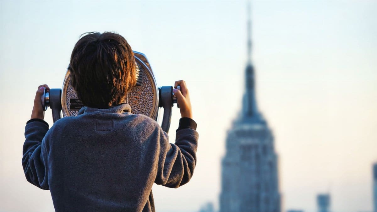 A child uses binoculars to view the Empire State Building in New York City at sunset.