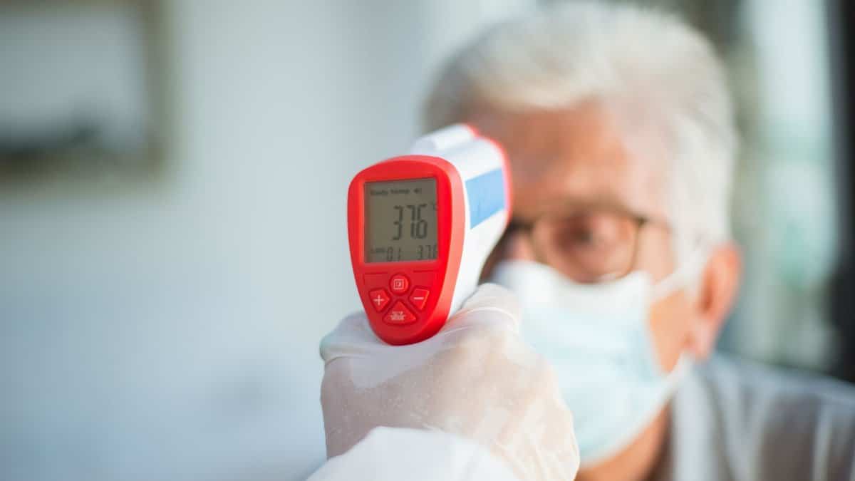 A healthcare professional uses a digital thermometer to check a senior patient's temperature indoors.