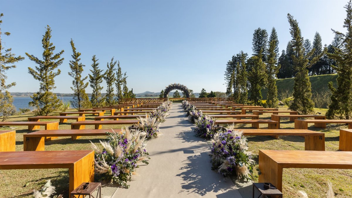 Charming outdoor wedding setup with wooden benches and floral decor by a serene lake.