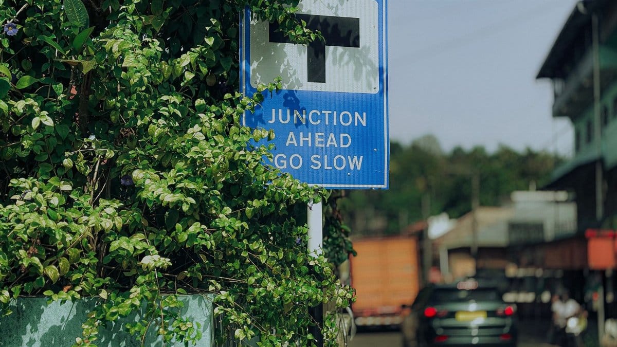 A T-junction traffic sign surrounded by foliage in Ernakulam, India, indicating caution.