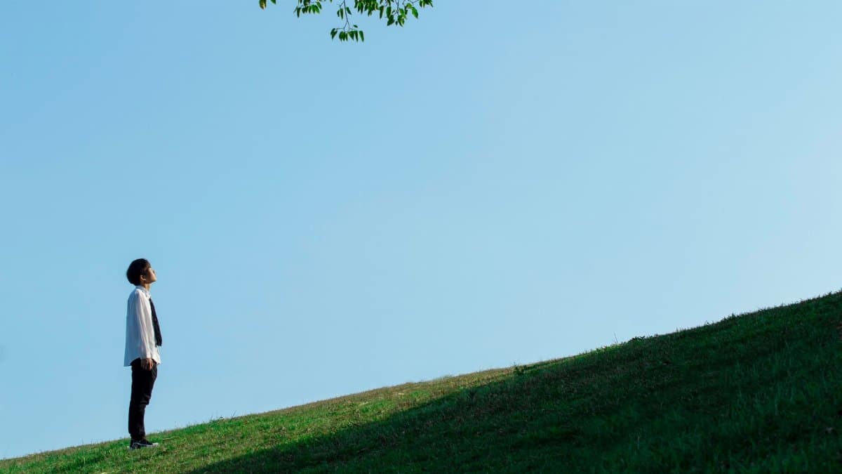 Adult male looking up while standing on a grassy hill under a clear sky.