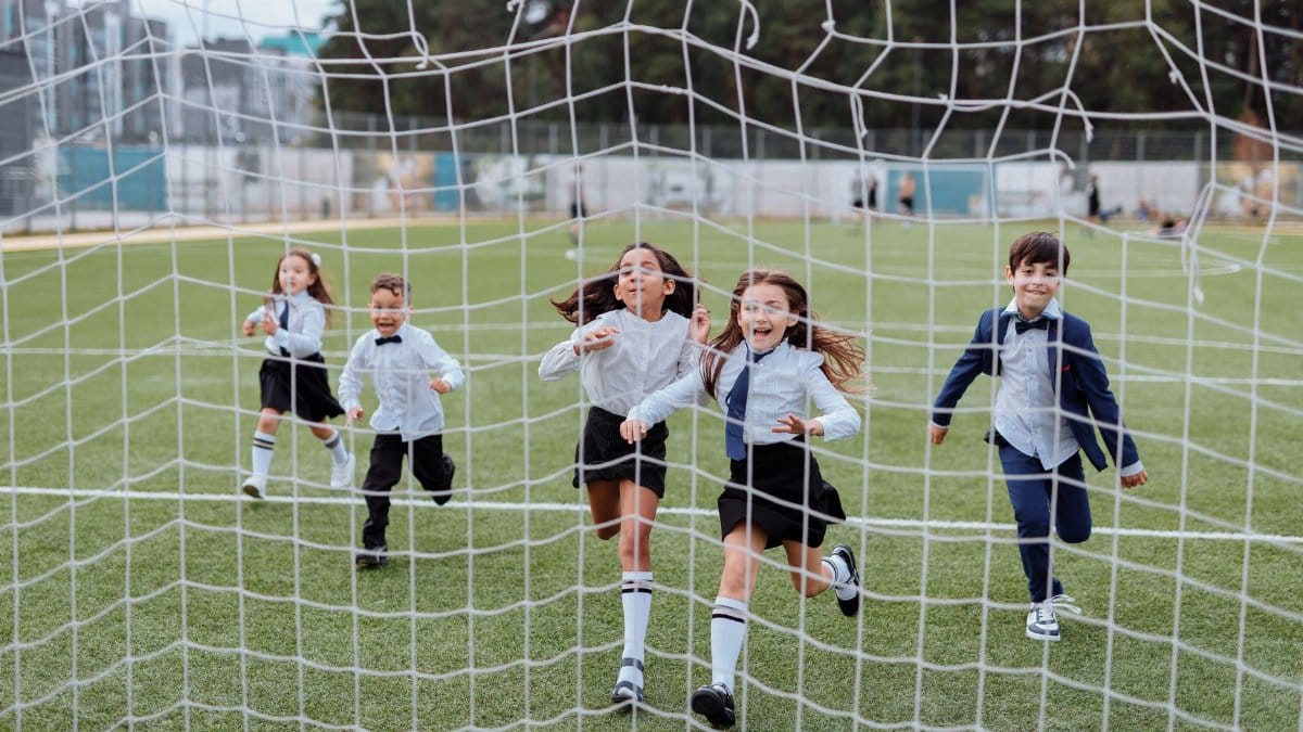Group of children joyfully running towards the camera on a soccer field, showcasing a lively and playful moment.