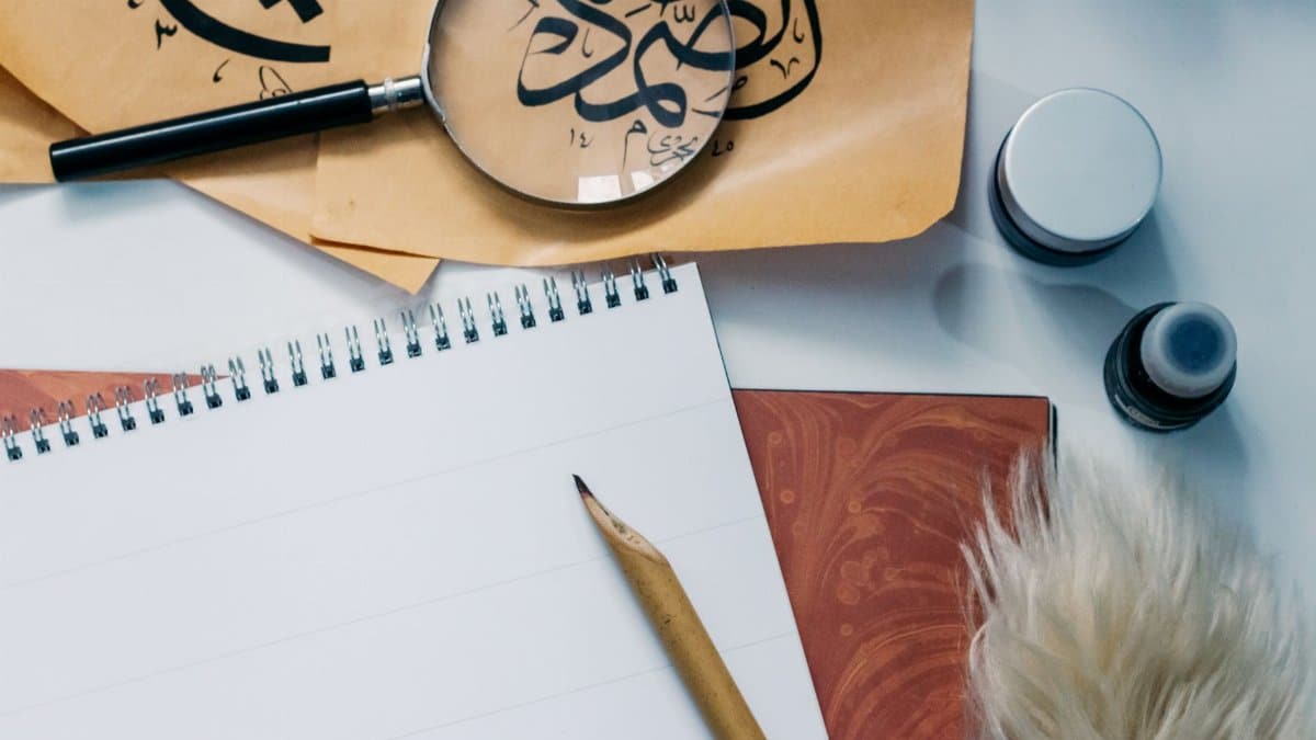 Artistic flat lay of calligraphy tools, notepad, and magnifying glass for creative inspiration.