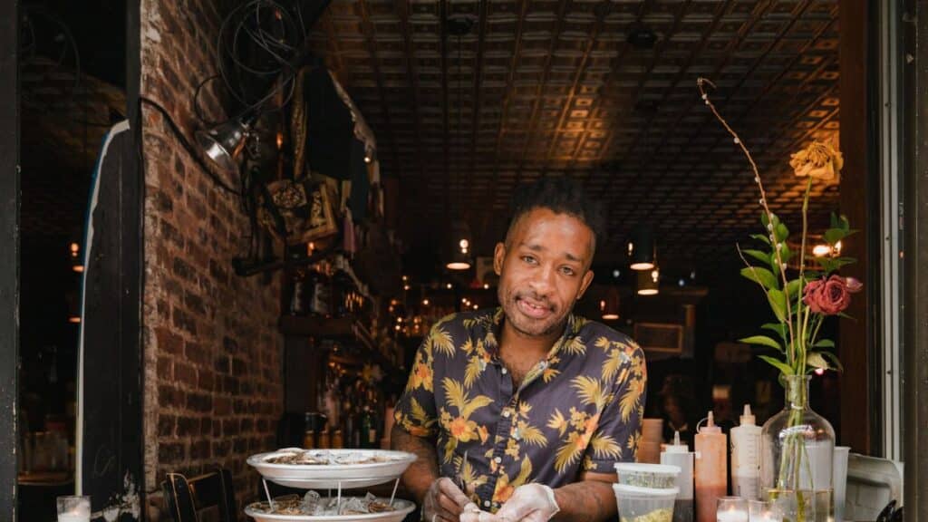 A man in a Hawaiian shirt prepares oysters at a restaurant counter, showcasing small business charm.