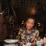 A man in a Hawaiian shirt prepares oysters at a restaurant counter, showcasing small business charm.