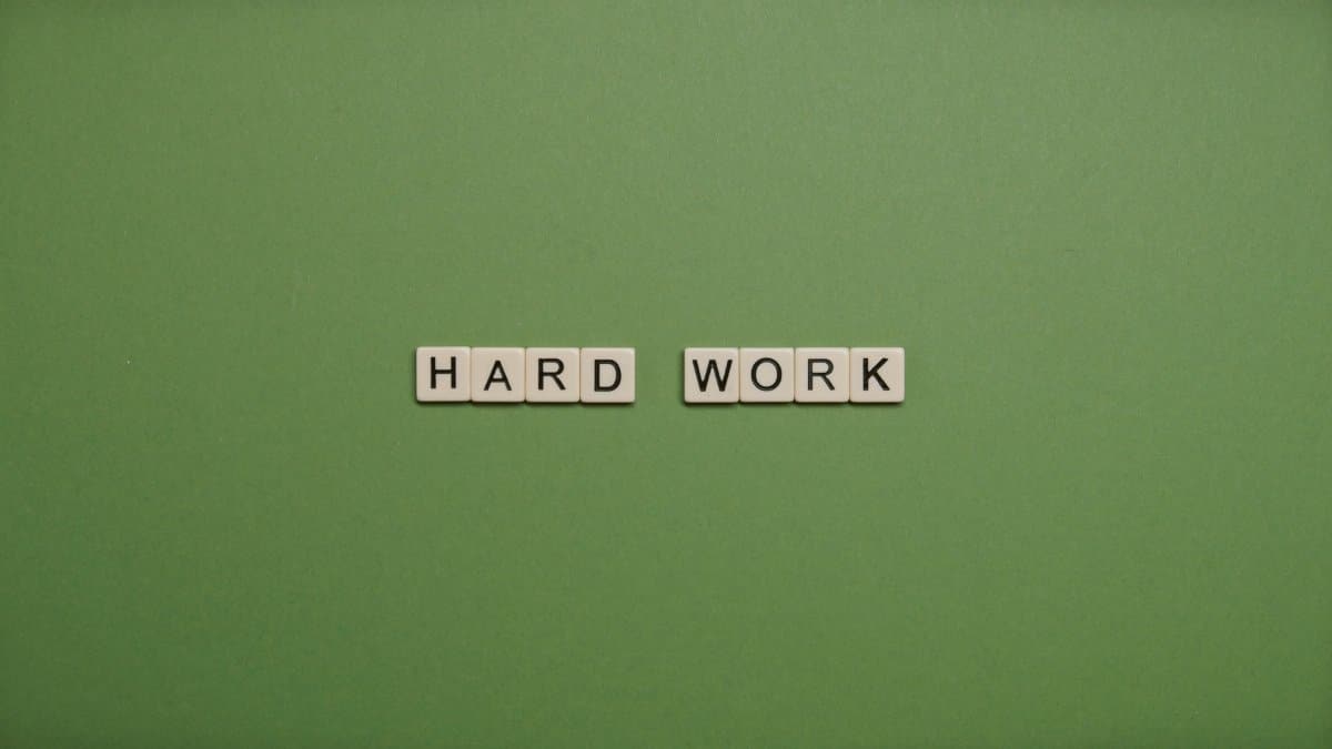 Tiles spelling 'hard work' on a green background symbolizing diligence and effort.