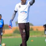 Goalkeeper throwing soccer ball during outdoor team training session.