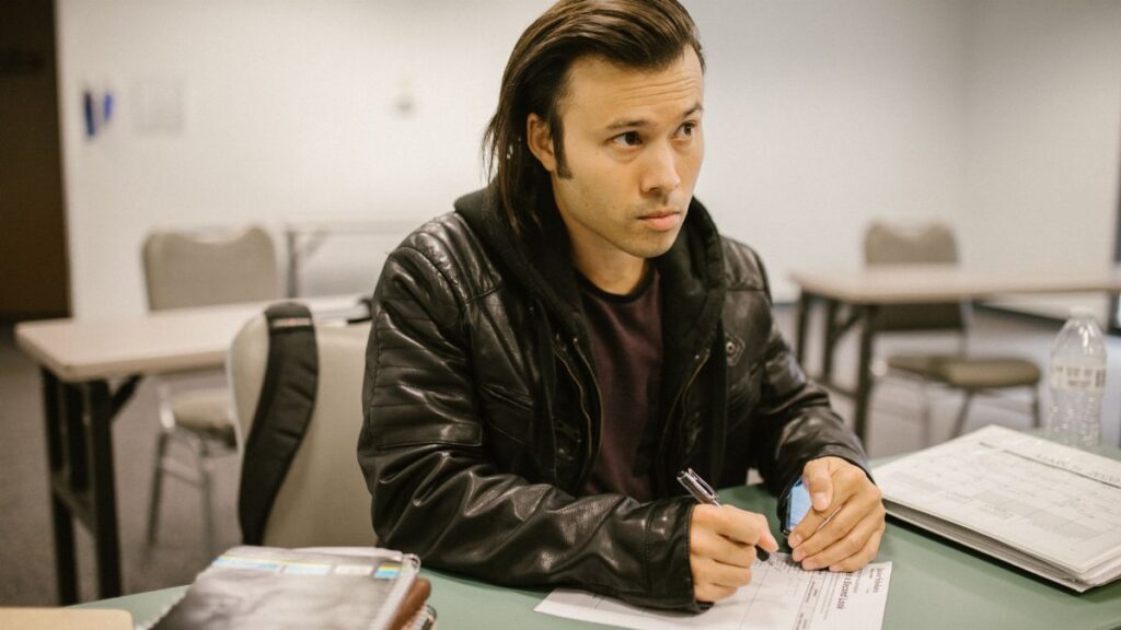 Focused student sitting at a desk during an exam in a classroom setting, writing on paper.