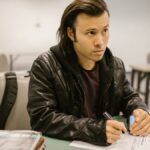 Focused student sitting at a desk during an exam in a classroom setting, writing on paper.