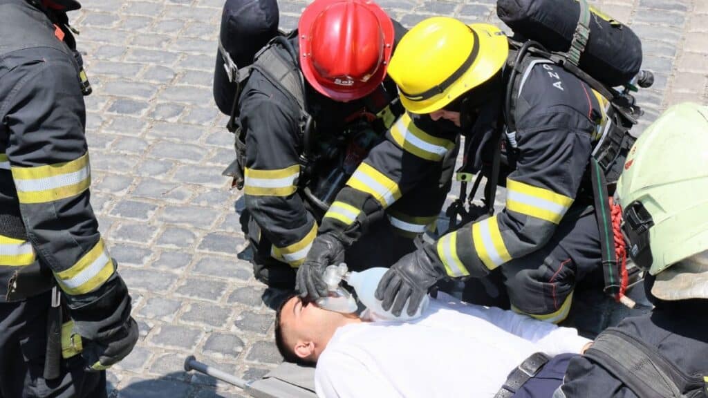 Firefighters provide CPR to an injured man using a bag valve mask on a cobblestone street.