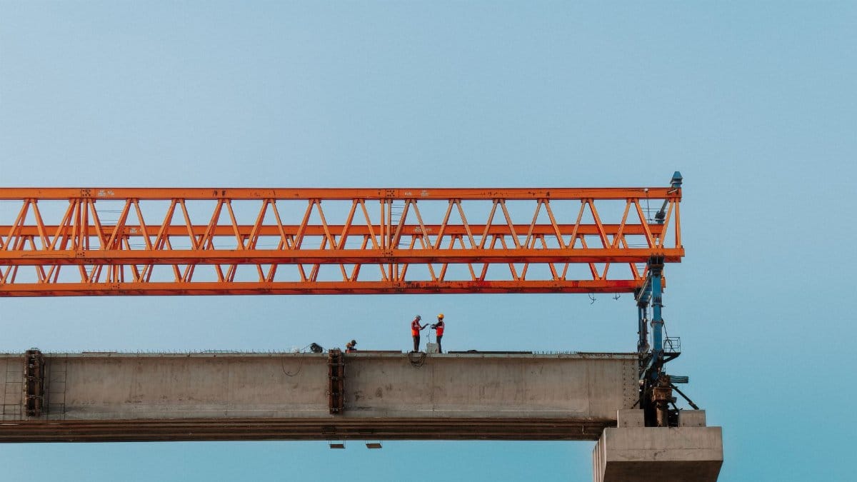 Construction workers on an elevated bridge in Chilmari, Bangladesh against a clear sky.