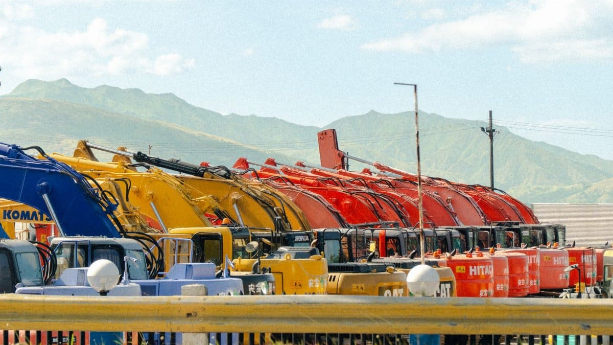 A lineup of vibrant construction vehicles against a beautiful mountain backdrop.