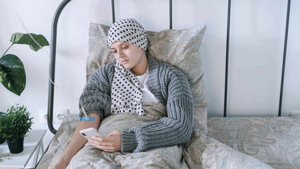 Woman undergoing cancer treatment at home, using a smartphone for support.