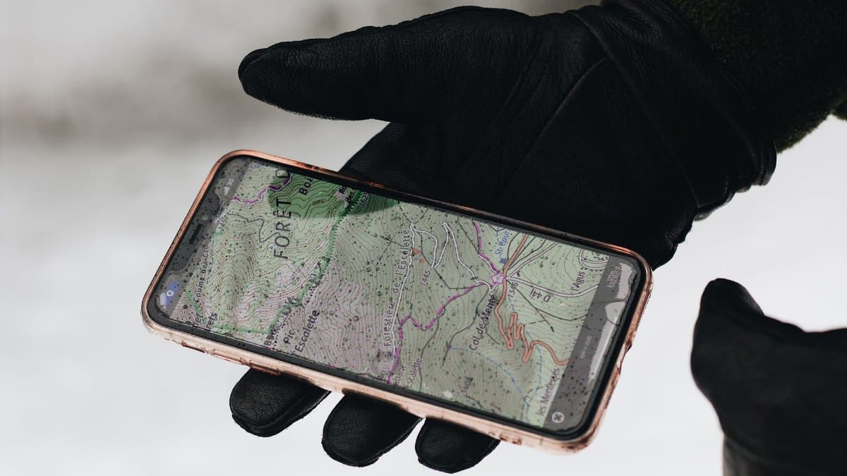 A gloved hand holds a smartphone with a map app displayed, showcasing navigation in cold weather.
