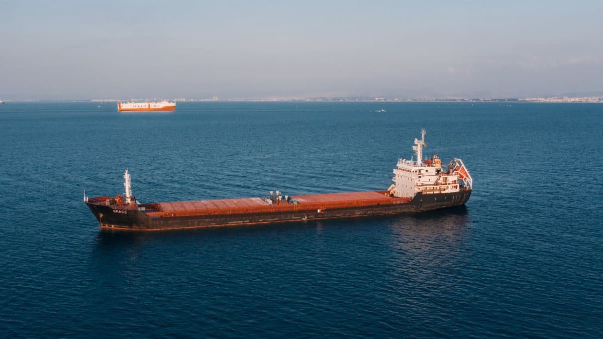 Aerial view of a cargo ship sailing in the open sea under clear skies, showcasing maritime transport.
