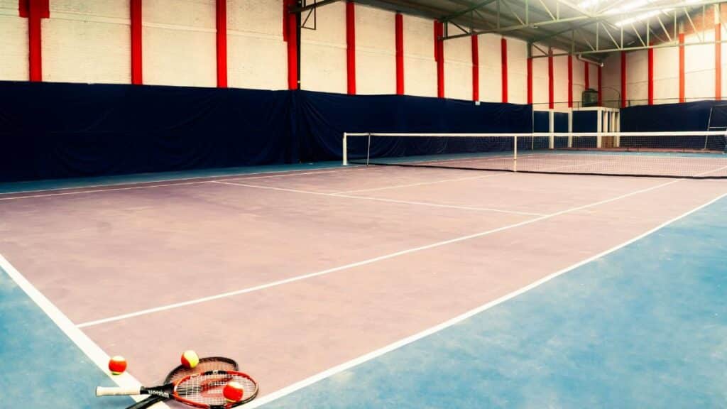 Empty indoor tennis court with rackets and balls in the foreground, showcasing a sports arena setup.