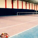 Empty indoor tennis court with rackets and balls in the foreground, showcasing a sports arena setup.