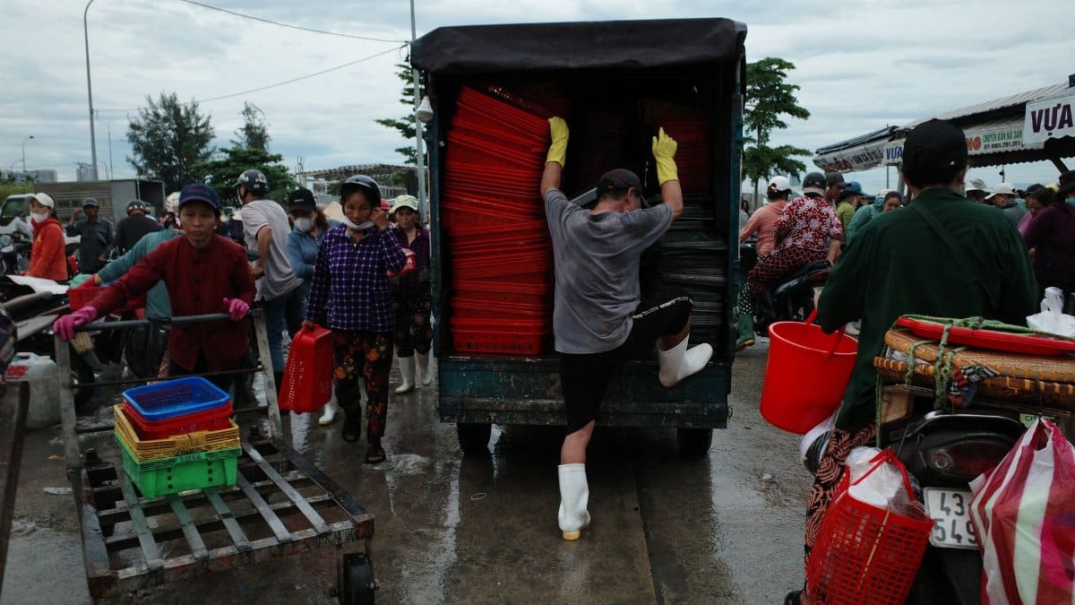 Busy scene at a local market with workers unloading colorful plastic bins from a vehicle.