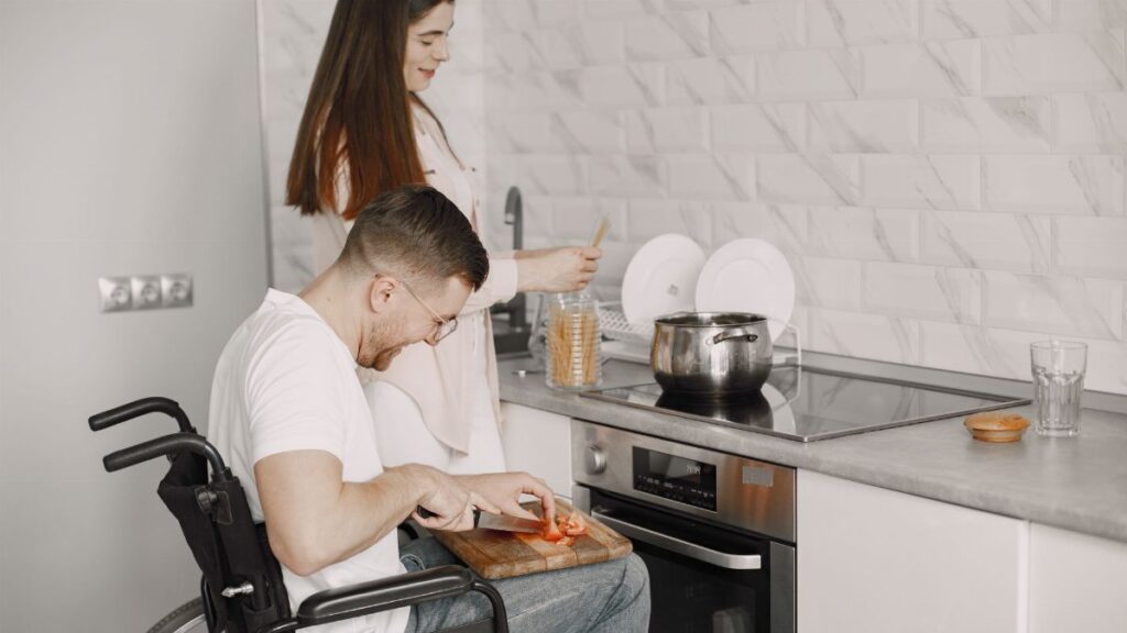 Man in wheelchair and woman cooking together in a stylish kitchen setting.