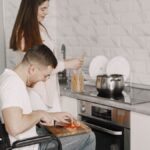 Man in wheelchair and woman cooking together in a stylish kitchen setting.