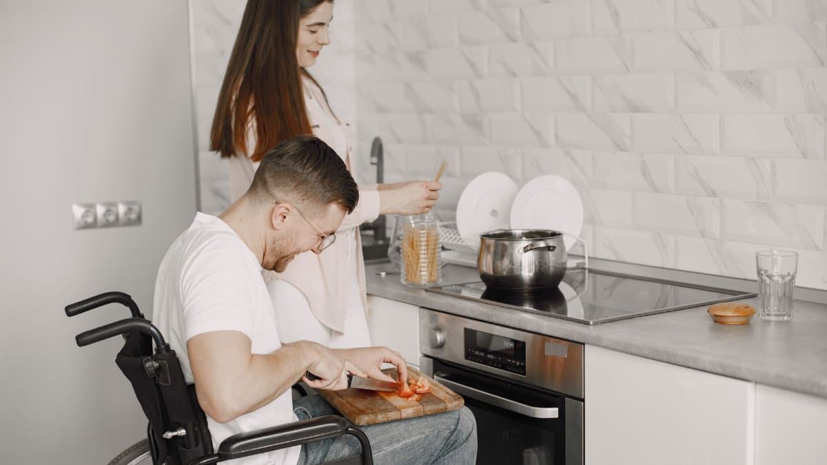 Man in wheelchair and woman cooking together in a stylish kitchen setting.