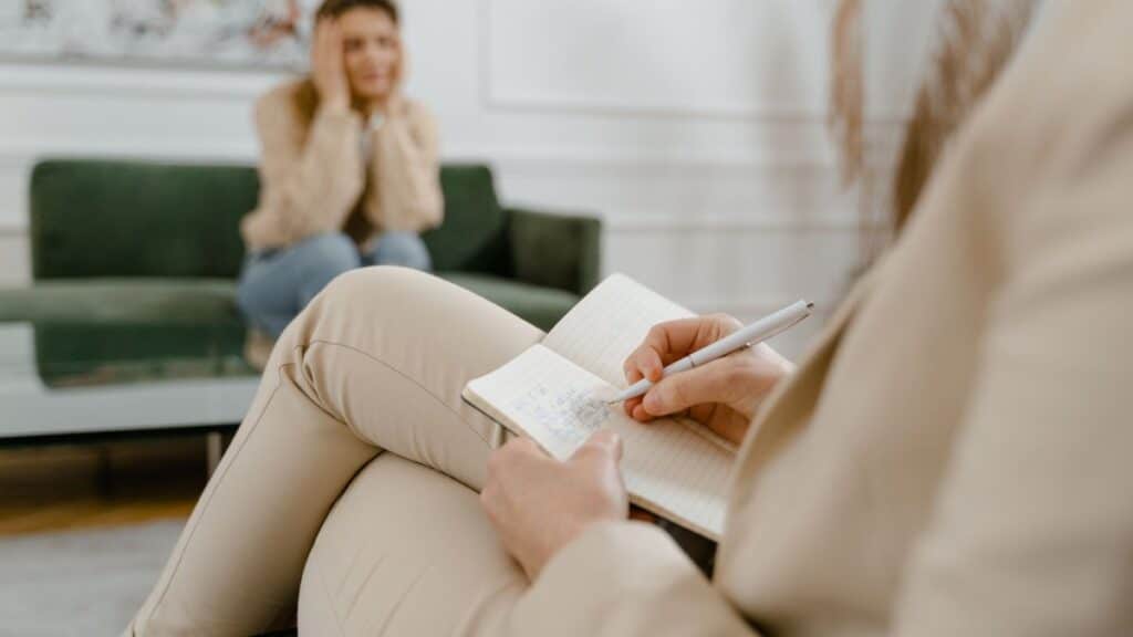 A therapist taking notes during a consultation with a patient, focusing on mental health.