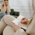 A therapist taking notes during a consultation with a patient, focusing on mental health.