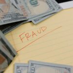 Close-up of US dollars and 'Fraud' written on yellow paper, representing financial scams.