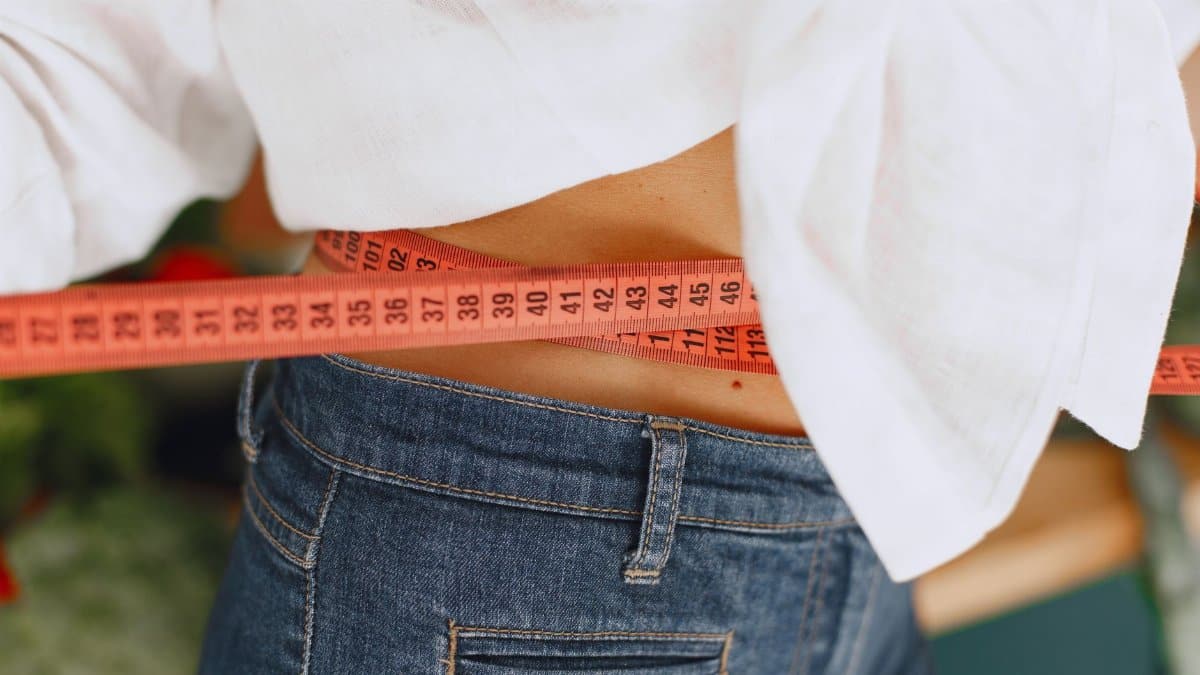 Close-up image of a woman measuring her waist with a tape measure, promoting fitness and health goals.