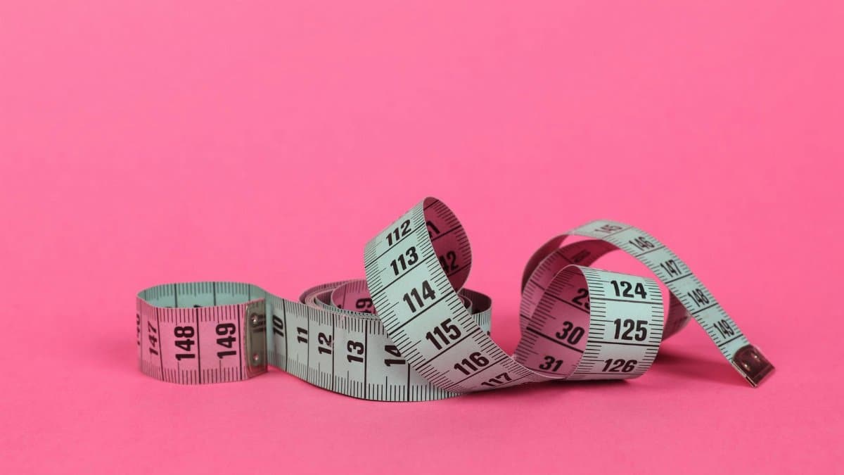 Close-up of a measuring tape on a vibrant pink background for design use.